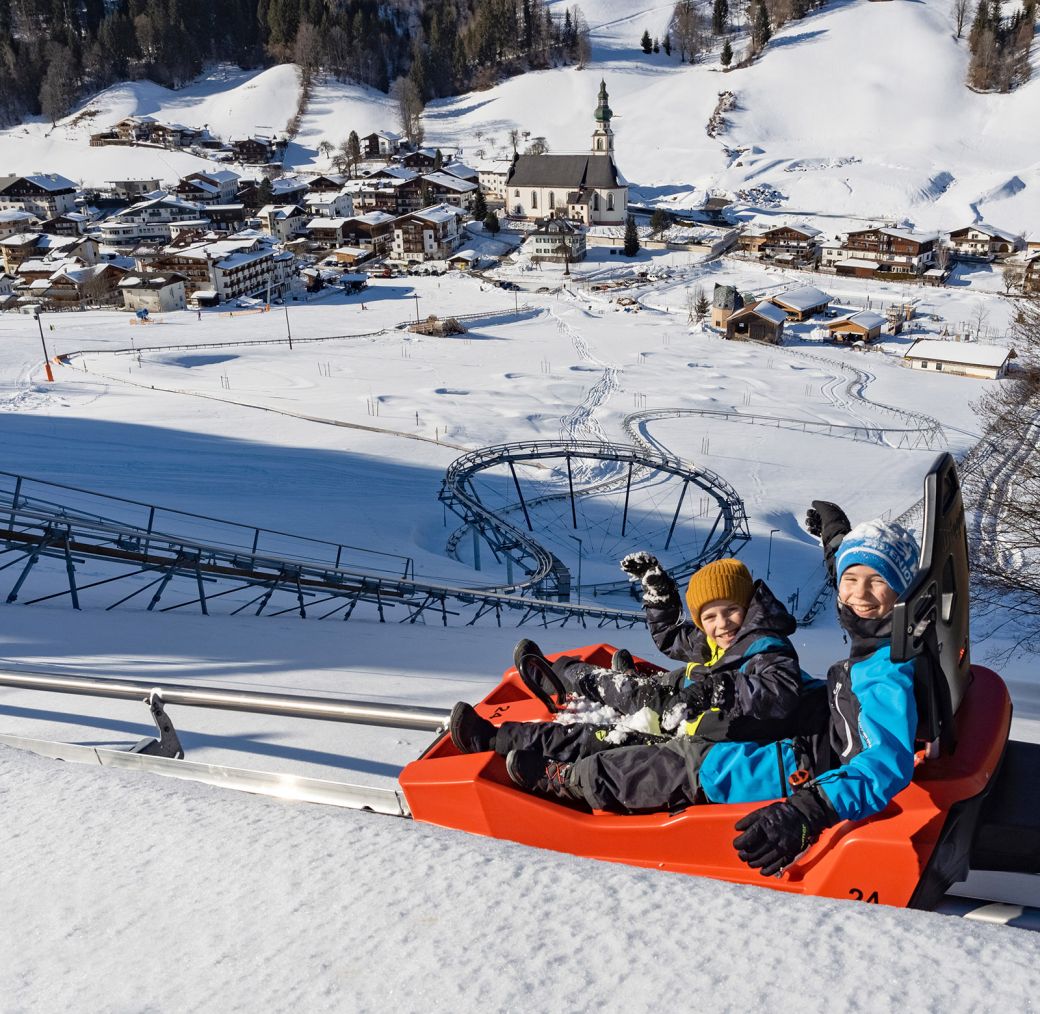 Children riding a winter alpine coaster through a snowy valley
