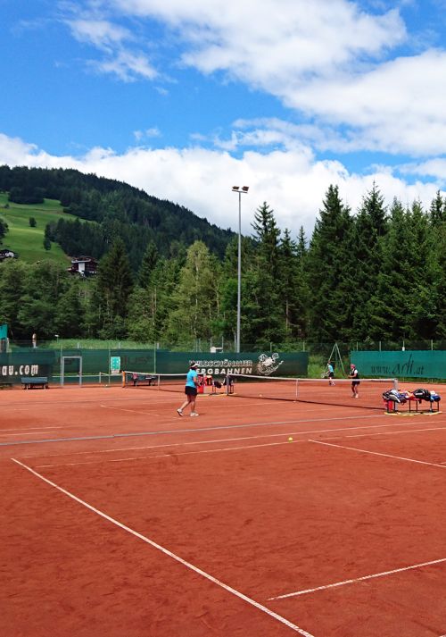 Tennis players on a clay court with alpine mountain scenery in the background