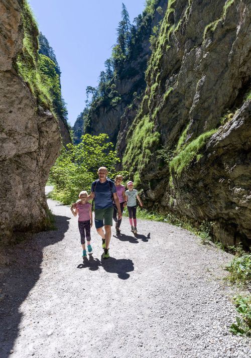 Family hiking through the Kundl Gorge with high rock walls and forest surroundings