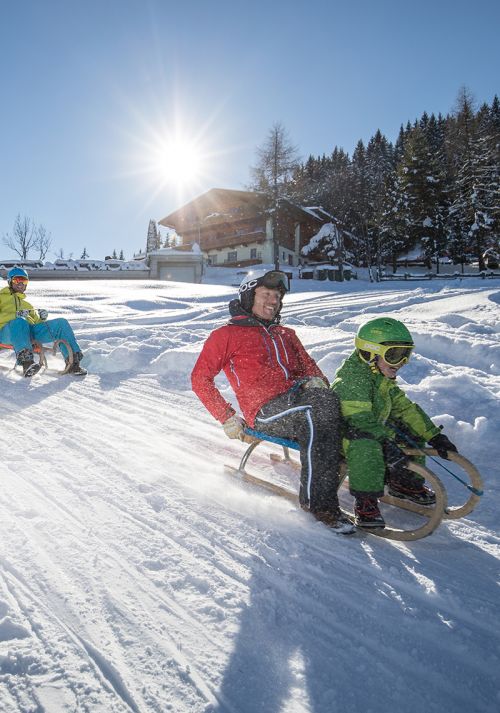 Family sledding on a sunny snow-covered toboggan run