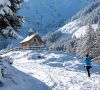 Winter hiker walking on a snowy path near a small mountain chapel