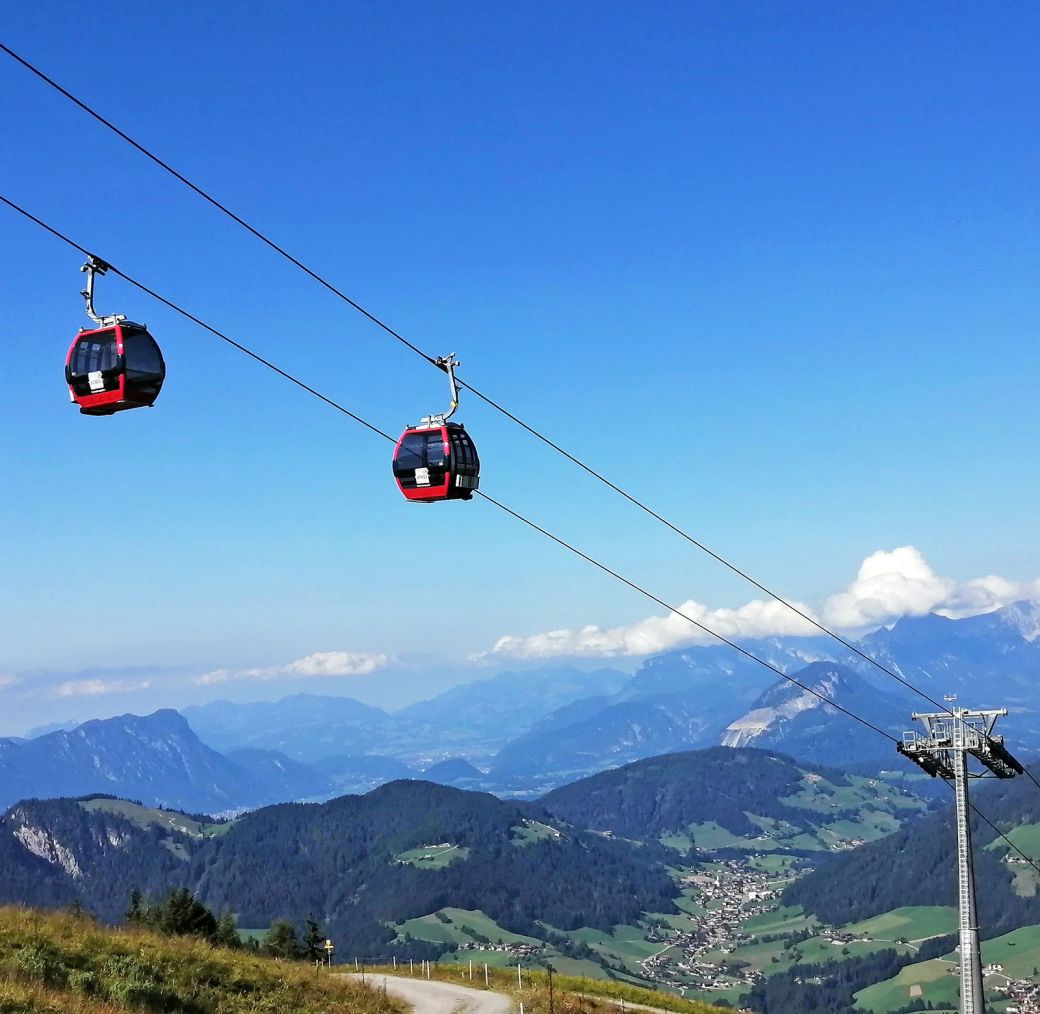 Red gondola cabins of the Schatzberg cable car above green alpine mountains with valley views
