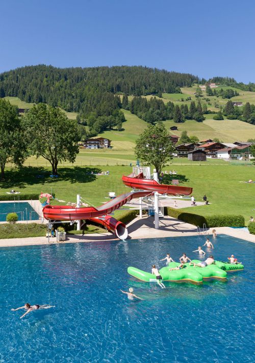 Outdoor swimming pool with water slide and sunbathing lawn set in a green mountain landscape