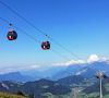 Red gondola cabins of the Schatzberg cable car above green alpine mountains with valley views
